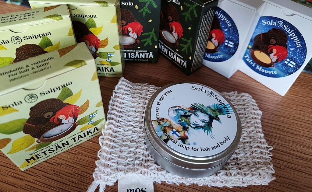 Erilaisia kartonkisia saippuapakkauksia, peltinen säilytysrasia ja pesupussi