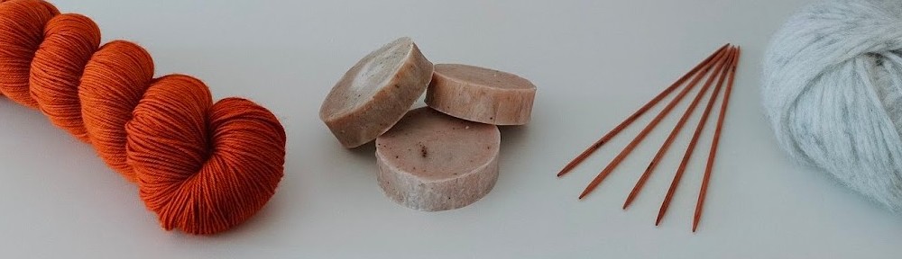Kuvassa oranssi lankavyyhti, pyöreitä saippuoita, puikot ja vaalea lankakerä