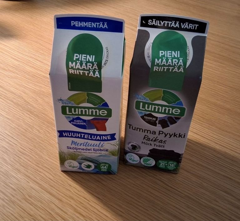 Kaksi kartonkista maitotölkin muotoista pakkausta, toinen tummalle pyykille ja toinen huuhteluainetta