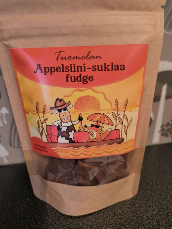 Tuomelan appelsiinisuklaa fudge pakkaus. Ruskeaa pahvia muistuttava pakkaus, jonka kannessa on animoidun lehmän ja ketun kuva.